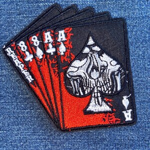 May include: A set of five black playing card patches with red and white accents. The cards feature the Ace of Spades and the eight of spades, with intricate embroidered details. The patches are arranged in a fanned-out pattern.