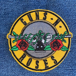 May include: Yellow and black embroidered patch with the words "Guns N' Roses" in a circle around a stylized image of a gun with roses.