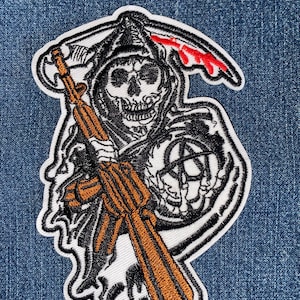 May include: Black and white embroidered patch of a hooded skeleton holding a rifle and an anarchy symbol. The skeleton is wearing a hooded robe with a red scythe.