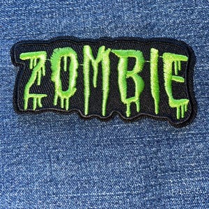May include: A black and green embroidered patch with the word "ZOMBIE" in dripping green letters.