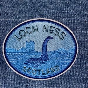 May include: An oval patch with a blue and white border, featuring the words "LOCH NESS SCOTLAND" in green and a depiction of the Loch Ness Monster in the water. The patch is on a denim background.