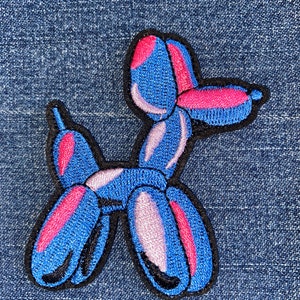 May include: A blue and pink balloon animal shaped like a dog. The balloon animal is embroidered on a denim fabric.