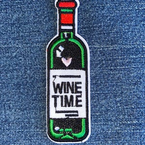 May include: Green and white embroidered iron-on patch of a wine bottle with the text "WINE TIME" on the label.