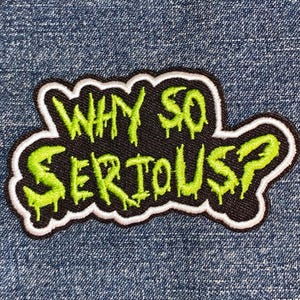May include: A black patch with the phrase "WHY SO SERIOUS?" in dripping neon green lettering. The patch has a white border and is set against a blue denim background. This patch is suitable for jackets, bags, or other fabric items.