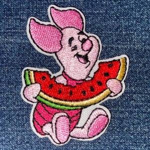 May include: An embroidered patch featuring a light pink cartoon pig character with large ears, holding a slice of red watermelon with black seeds, a green rind, and a yellow border, outlined in white thread against a blue denim fabric background.