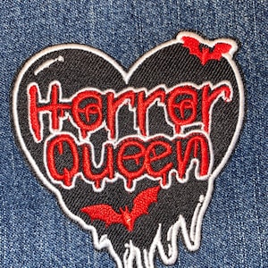 May include: Black heart-shaped patch with dripping edges, embroidered with the text "Horror Queen" in red and two red bats.