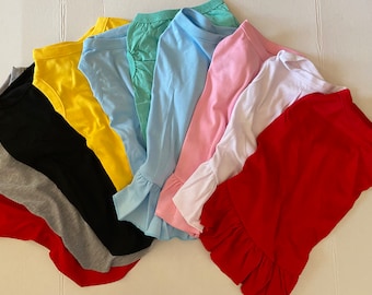 May include: A stack of eight ruffle-trimmed t-shirts in various colors, including red, yellow, black, gray, light blue, teal, pink, and white.