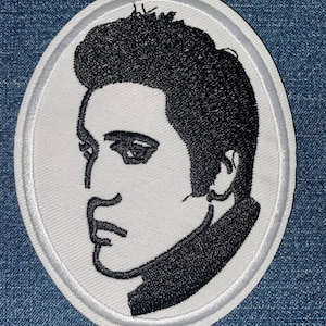 May include: Oval-shaped embroidered patch featuring a black and white profile of a person with a distinctive hairstyle. The patch has a white background with a black outline and is likely for clothing or accessories.