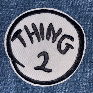 May include: A white circular patch with a black border and the text "THING 2" in black embroidery.