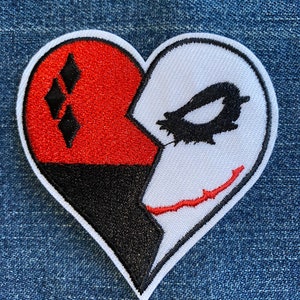 May include: A red, black, and white heart-shaped patch with a diamond pattern on the left side and a Joker-like face on the right side.