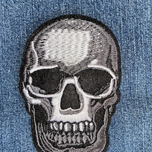 May include: A black and white embroidered skull patch. The skull has a detailed design with a white outline and black shading.