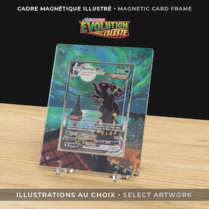 Peut inclure: Un cadre magnétique illustré avec une carte Pokémon représentant une créature noire et violette. Le cadre affiche le texte "EVOLUTION CELESTE" et "ILLUSTRATIONS AU CHOIX". Le cadre est soutenu par des supports en plastique transparent.