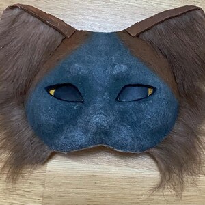 May include: A blue cat mask with brown fur ears. The mask has yellow eyes and a textured surface.