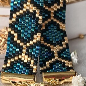 Pu&ograve; includere: Un bracciale in perline intrecciate con un motivo geometrico realizzato in perline di vetro color oro metallizzato, nero profondo e verde acqua iridescente. Presenta terminali in metallo dorato e una chiusura a catena scorrevole con perla.
