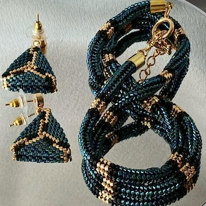 Pu&ograve; includere: Un set di gioielli composto da due orecchini a lobo triangolari e una collana abbinata a corda. I pezzi sono realizzati con piccole perline iridescenti blu petrolio scuro e nere con accenti dorati e componenti in metallo color oro.