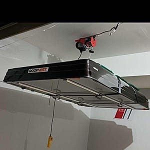 May include: A black ceiling-mounted storage system with the text "Roofnest" on the front. The system is suspended from the ceiling with a red electric winch and a yellow remote control.
