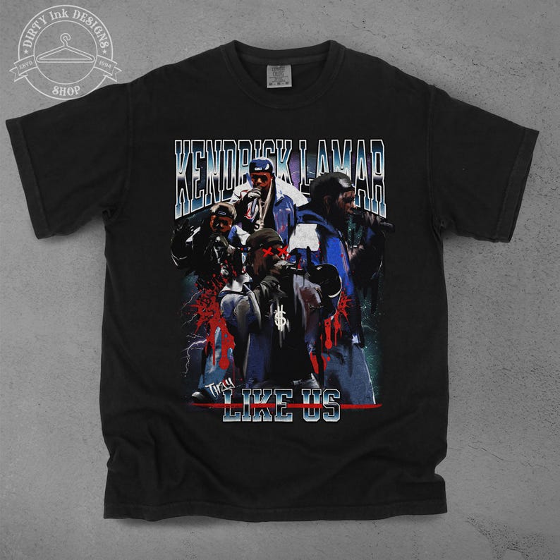Op de afbeelding: Zwart T-shirt met een vintage-stijl grafische afbeelding met een groep mannen met de tekst "Kendrick Lamar" en "They Like Us" gedrukt op de voorkant.