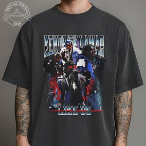 Op de afbeelding: Zwart T-shirt met een vintage-stijl afbeelding van Kendrick Lamar en de woorden "They Like Us".