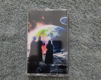 May include: A cassette tape with a colorful image of three figures standing on a moon-like surface, looking at a glowing Earth in the background.
