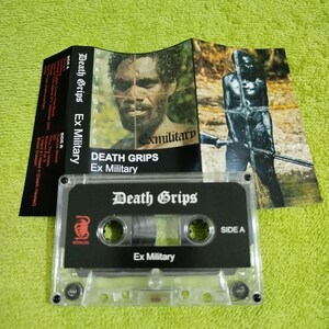 May include: A clear cassette tape with a black label. The label has the text "Death Grips" in white and "Ex Military" in black. The cassette tape is in a clear plastic case.