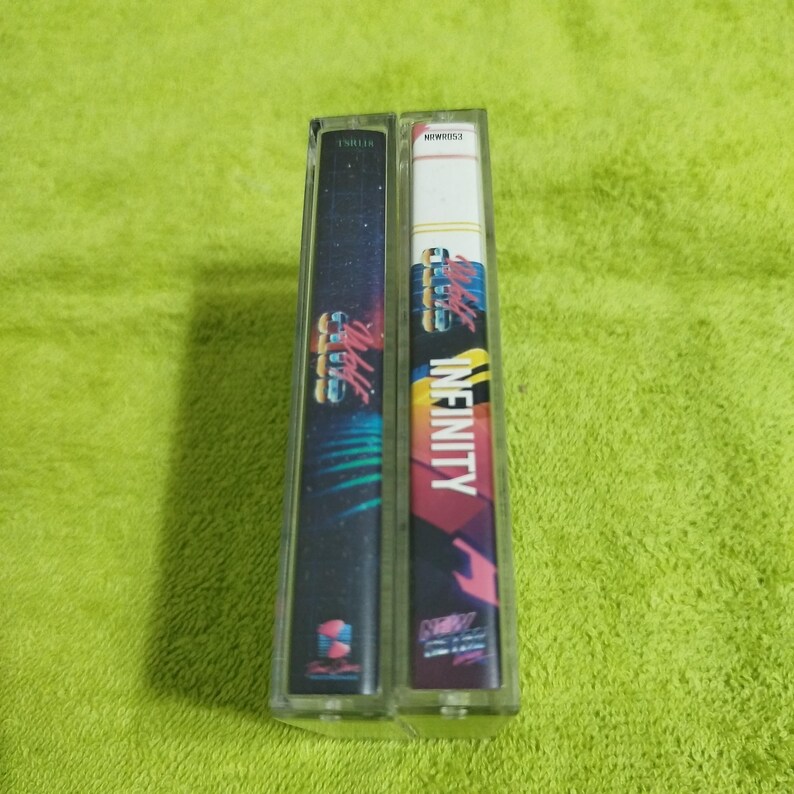 May include: Two cassette tapes with colorful designs. The tape on the left has a black background with a blue and green design and the text "Infinity" in white. The tape on the right has a pink background with a blue and yellow design and the text "Infinity" in white.