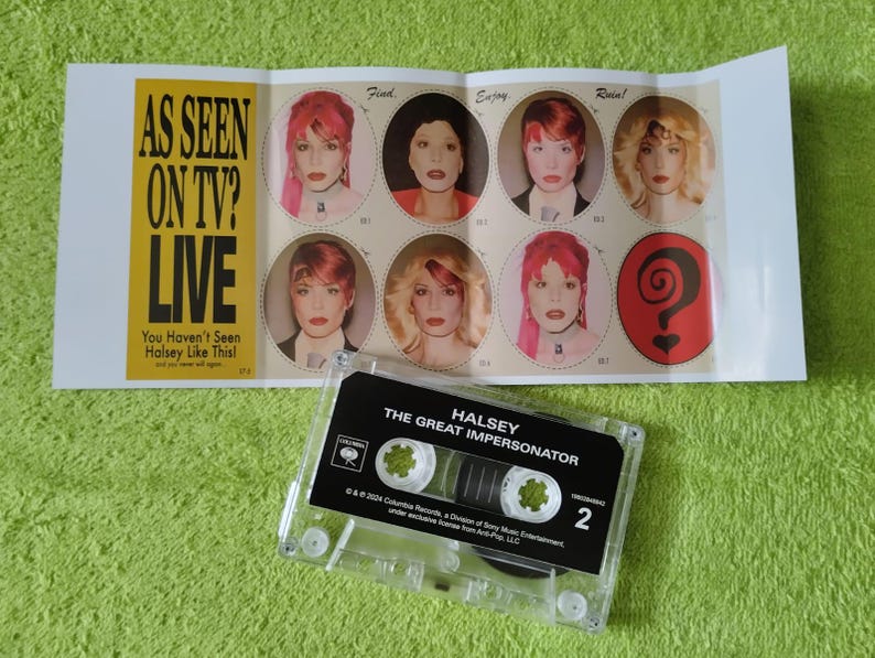 May include: A clear cassette tape labeled "Halsey The Great Impersonator" sits below a folded card with images of Halsey and the text "AS SEEN ON TV? LIVE". The card has a yellow and black color scheme.
