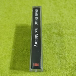 May include: A black cassette tape with the text "Death Grips Ex Military" printed on the label.