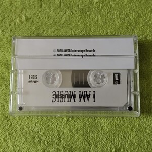 May include: A clear cassette tape with the words "I AM MUSIC" printed on the label. The tape is in a clear plastic case, and the background is a green surface. The text "SIDE 1" is also visible.