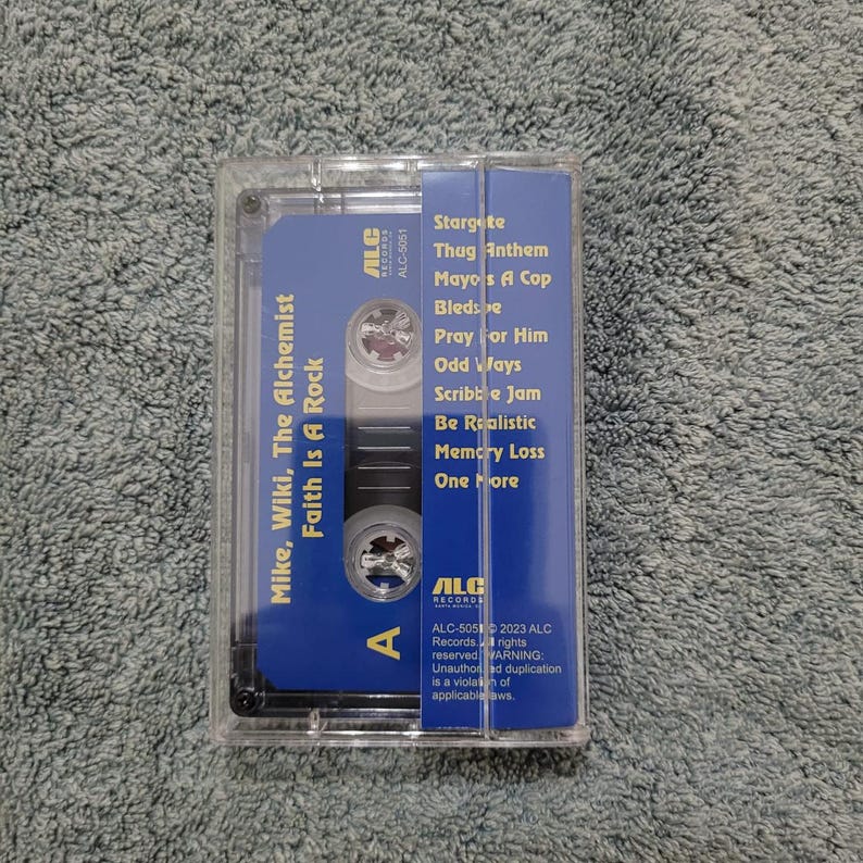 May include: A blue and black cassette tape with the title "Mike, Wiki, The Alchemist Faith Is A Rock" and the tracklist: "Stargete", "Thug Anthem", "Mayo's A Cop", "Bledse", "Pray For Him", "Odd Ways", "Scribble Jam", "Be Realistic", "Memory Loss", "One More".