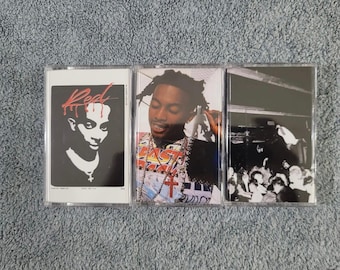 May include: Three cassette tapes with different covers. The first tape has a black and white image of a person's face with the word "Red" written in red above the face. The second tape has a color image of a person wearing a colorful shirt and a silver chain with a cross pendant. The third tape has a black and white image of a crowd of people.