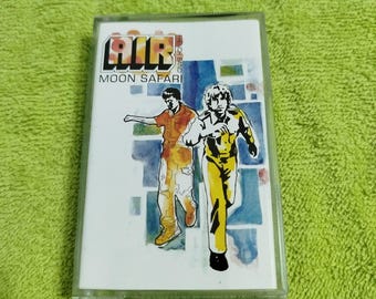 May include: A cassette tape featuring a watercolour illustration of two people running. The tape is labelled "AIR" and "MOON SAFARI".