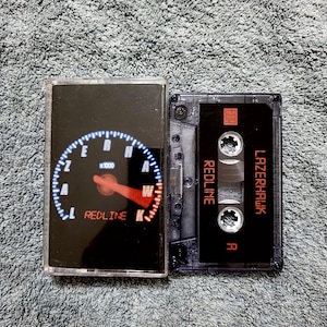 Può includere: Un nastro audio nero con una grafica di tachimetro rosso e bianco sul davanti. Il nastro è etichettato "Lazerhawk" e "Redline".