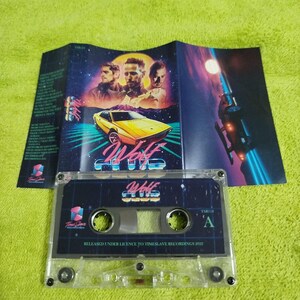 May include: A clear cassette tape with a black and blue label that says "Wolf Club" and "TMS110 A". The label has a retro 80s design with a yellow car and a futuristic spaceship. The text "Released under licence to Timeslave Recordings 2022" is printed on the label.