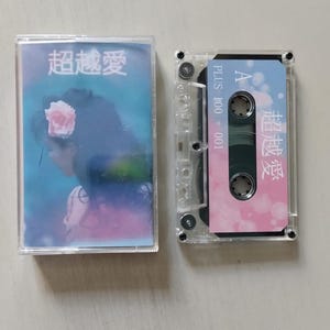 May include: A clear cassette tape with a pink and blue design. The tape has the text "PLUS 100 + 001" and "A" on the side. The front of the tape has the text "超越愛" in pink and white.