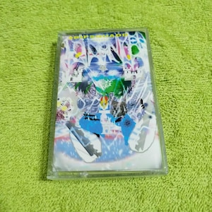 Peut inclure: Une cassette audio avec un design abstrait coloré. La cassette est dans un boîtier en plastique transparent et porte l'inscription "TRIPSIDAD" sur le devant.