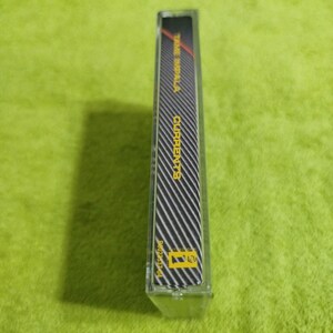 May include: A clear cassette tape case with a black and white striped design. The text "TAME IMPALA CURRENTS" is visible in red and yellow. The case is on a green surface.