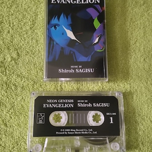 May include: Two clear cassette tapes of "Neon Genesis Evangelion" music by Shiroh Sagisu. The top cassette features a blue-toned anime illustration. The bottom cassette has a black label with white text and a Star Child logo.