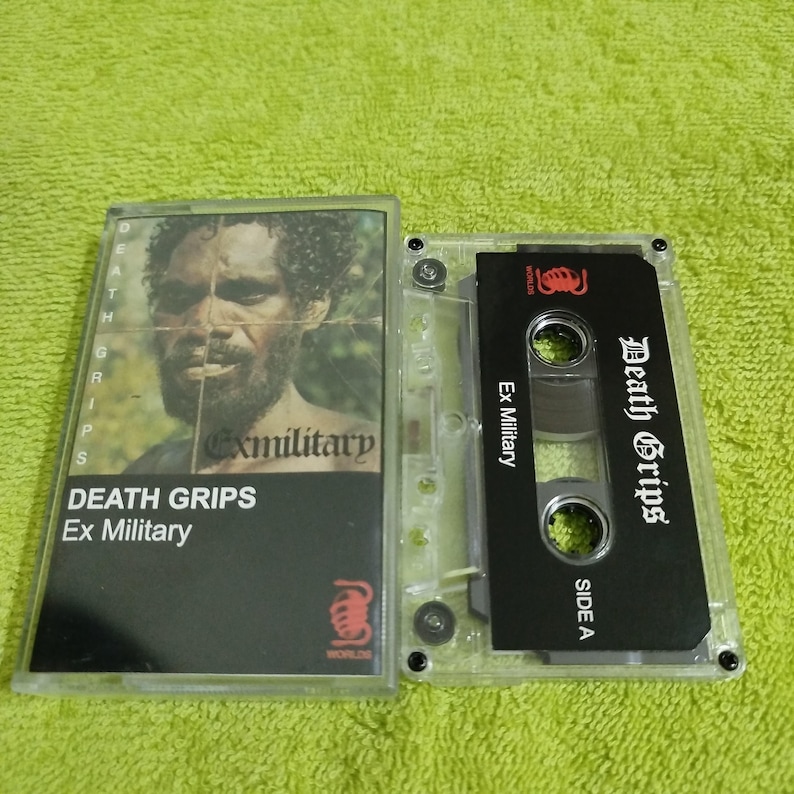 May include: A black cassette tape with the title "Death Grips" and "Ex Military" printed on the label. The tape is in a clear plastic case.