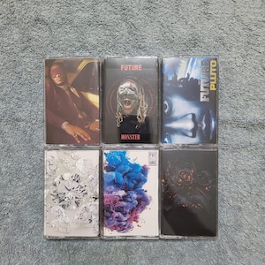 May include: Six cassette tapes with different album covers. The covers feature a man wearing a blindfold, a man with a monster mask, a man with a blue face, a pile of diamonds, a blue and purple cloud, and a black rose.