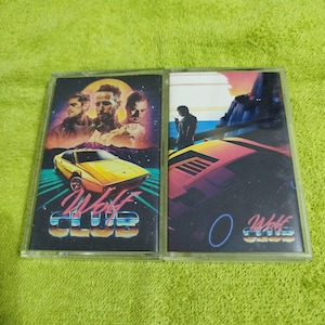 May include: Two cassette tapes with a retro 80s design. The front of each tape features a yellow sports car, a sunset, and the text "Wolf Club". One tape features three men in the background, while the other features a single man.