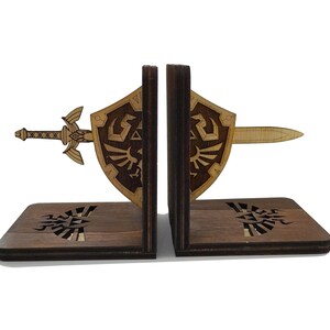 Peut inclure: Des serre-livres en bois en forme d'épée de maître et de bouclier hylien de la série de jeux vidéo The Legend of Zelda. Les serre-livres sont de couleur marron avec un motif en bois clair.