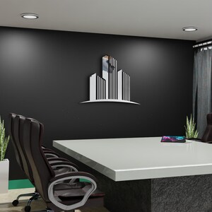 May include: A modern office setting featuring a large white conference table with a dark gray base. Black leather office chairs surround the table. A stylized building logo is mounted on the black wall. Green plants and gray curtains add to the decor.