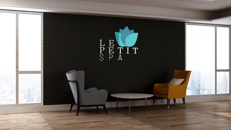 May include: Interior shot of a spa waiting area with a black accent wall. The wall features the text "LE PETIT SPA" and a blue and teal lotus flower logo. Two armchairs, one gray and one yellow, and a round table are in front of the wall.