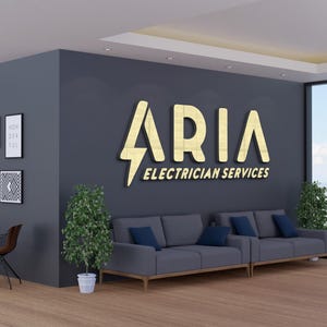 May include: Interior shot of an office space with a dark gray wall featuring a gold sign that reads "ARIA ELECTRICIAN SERVICES." A gray sofa with blue pillows sits below the sign. Decorative framed art hangs on the wall. A table and chairs are in the foreground.