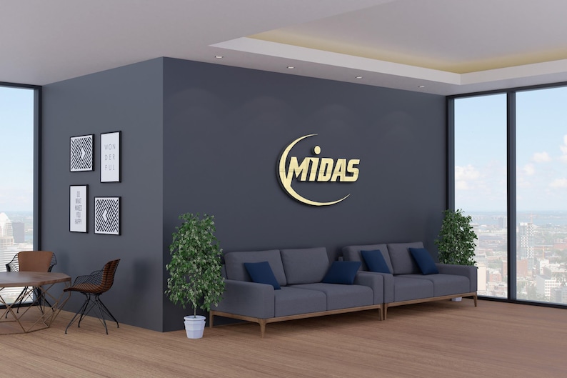 May include: Interior shot of a modern office space with a gray wall featuring a gold "MIDAS" logo. Two gray sofas with blue cushions are in front of the wall. Decorative framed art and plants add to the decor.