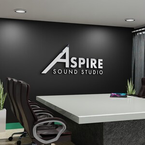 May include: A modern conference room with a large white table and black leather chairs. The wall features the text "ASPIRE SOUND STUDIO" in silver lettering. Two potted plants and a tablet are on the table.