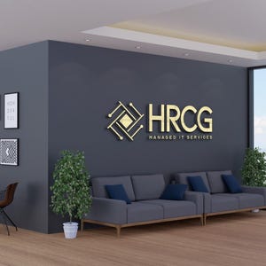 May include: An office interior with a modern design. The room features a dark gray wall with a gold logo that reads "HRCG Managed IT Services." There are two gray sofas with blue cushions, framed artwork, and potted plants. Large windows offer a city view.