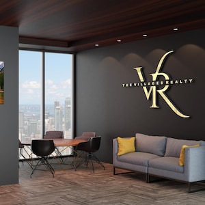 May include: An interior office space with a modern design. The room features a gray sofa with yellow pillows, a round wooden table, and black chairs. The wall displays a gold logo for "The Villages Realty."