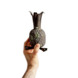 Puede incluir: Un objeto decorativo vintage de metal con forma de piña con un acabado desgastado. La piña es marrón y verde con un diseño detallado.