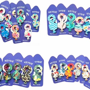 Op de afbeelding: Assortiment van kleurrijke nagelbeschermers met verschillende patronen, waaronder bloemen, dierenprint en geometrische ontwerpen. Elke nagelbeschermer is verpakt op een paarse kaart met de merknaam "KEYSIE" en de tekst "Nail Saver".